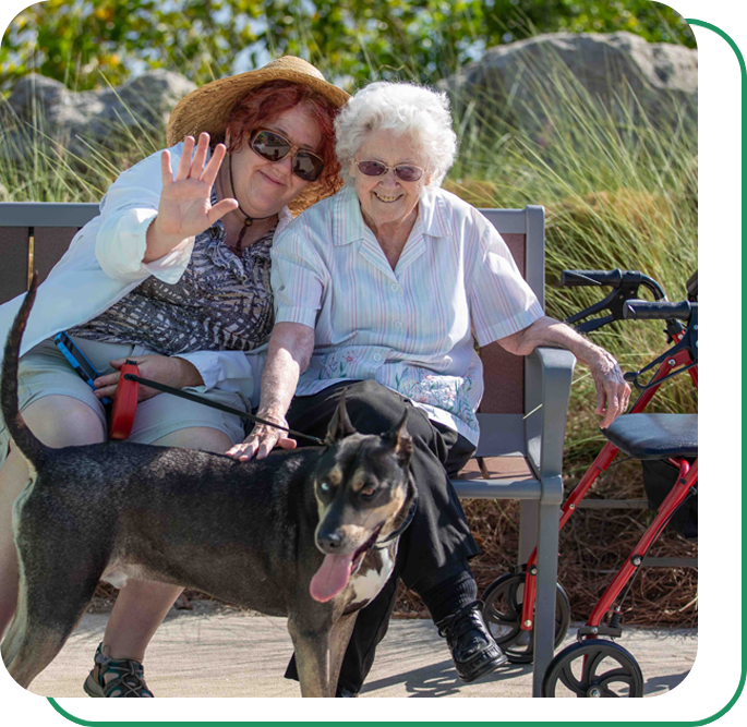 Two older woman sitting on a park bench with their dog